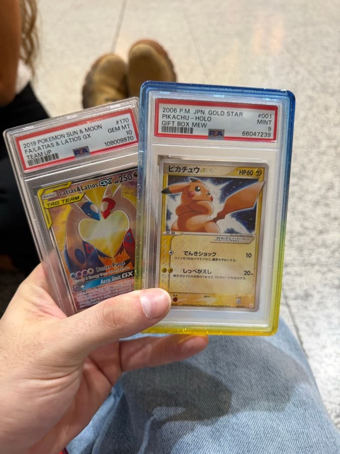 Two PSA-graded Pokémon cards held in hand: JP Pikachu Gold Star PSA 9 and Latias & Latios GX PSA 10